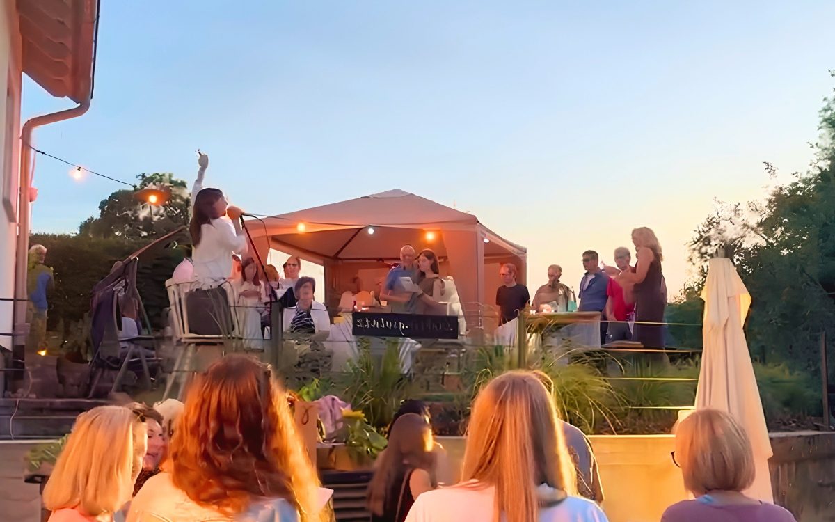 Luisa Loreen bei einem Mitsingevent unter freiem Himmel, das Publikum sitzt an Tischen davor.