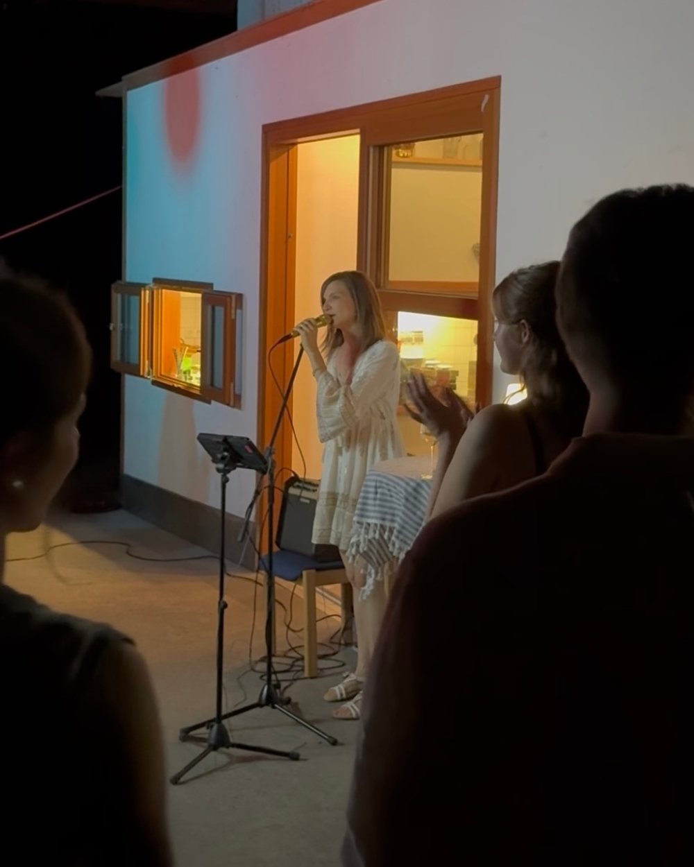 Luisa Loreen singt abends vor einer beleuchteten Hauswand; im Vordergrund sitzen Gäste mit dem Rücken zur Kamera, eine Person applaudiert.