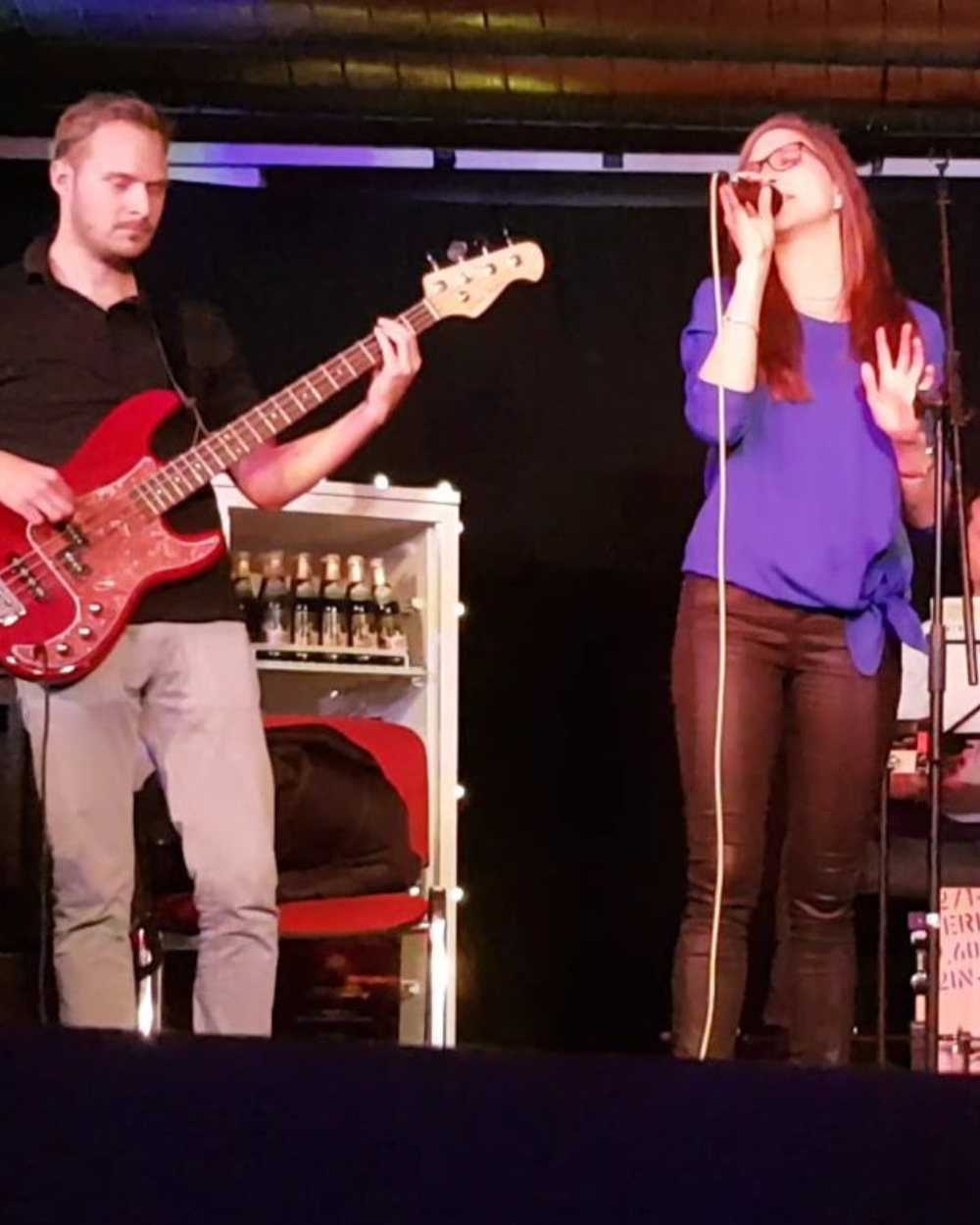 Luisa Loreen singt in blauer Bluse mit Handmikrofon auf einer Bühne, links von ihr ein Bassist mit roter E-Bassgitarre.