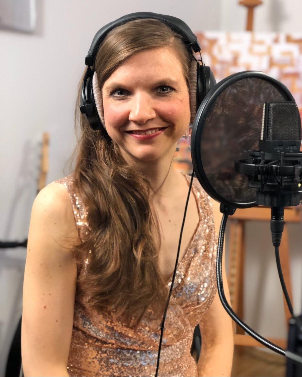 Luisa Loreen mit Kopfhörern und goldglänzendem Kleid lächelt neben einem Studiomikrofon mit Popschutz.