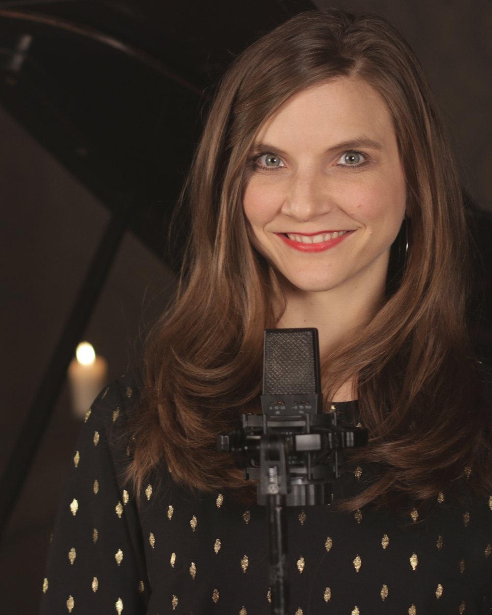 Porträt von Luisa Loreen hinter einem Studiomikrofon; im Hintergrund ein Flügel und eine brennende Kerze.